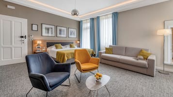 A hotel room with a bed, two armchairs, a sofa, a coffee table, and a desk with a lamp.