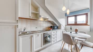 A modern kitchen with white cabinetry, a built-in oven, and a dining area with a table and chairs.