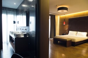 A modern hotel room with a large bed, a bedside table, a built-in desk, and a large mirror.