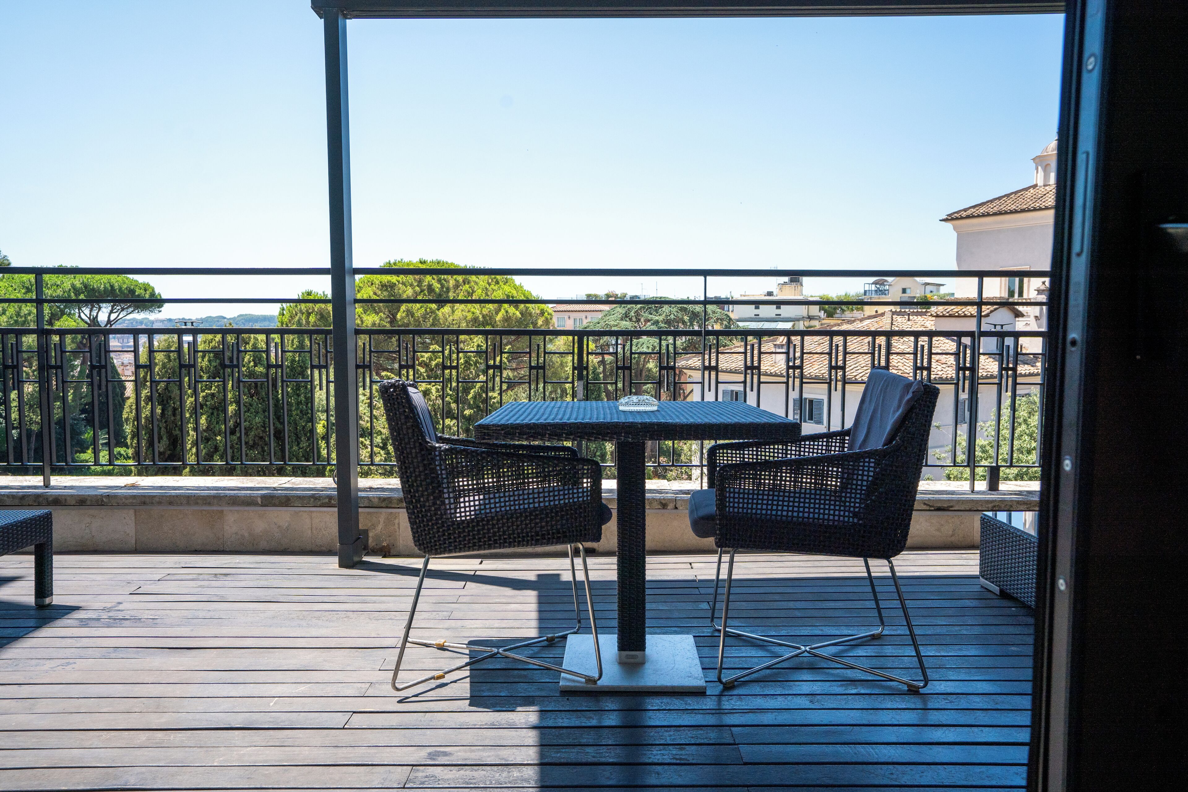 Uma varanda com mesa e cadeiras, um banco e vista para edifícios e árvores.