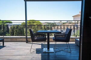 Een balkon met een tafel en stoelen, een bankje en uitzicht op gebouwen en bomen.