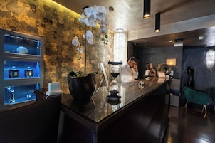 A bar area with a decorative orchid, an hourglass, and a wine bottle. There are shelves with bottles and a chandelier in the background.