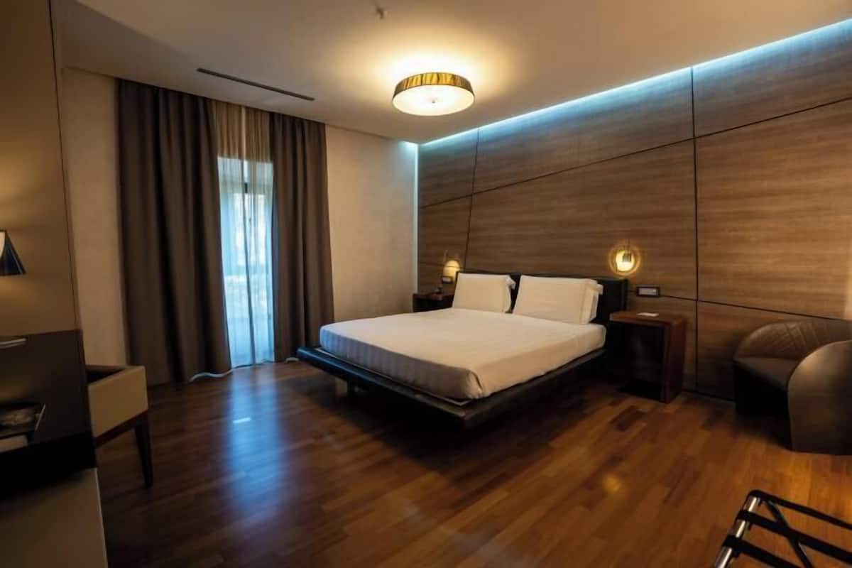 A modern hotel room with a large bed, wooden panel walls, a desk, and a chair.
