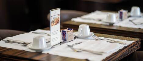 A dining area with tables set for service, including white plates, cups, and cutlery.