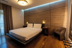 A modern hotel room with a large bed, wooden panel walls, and a small seating area.