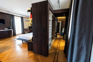 A modern hotel room with a wooden floor, a bed, a desk with a chair, a TV, and a wardrobe.