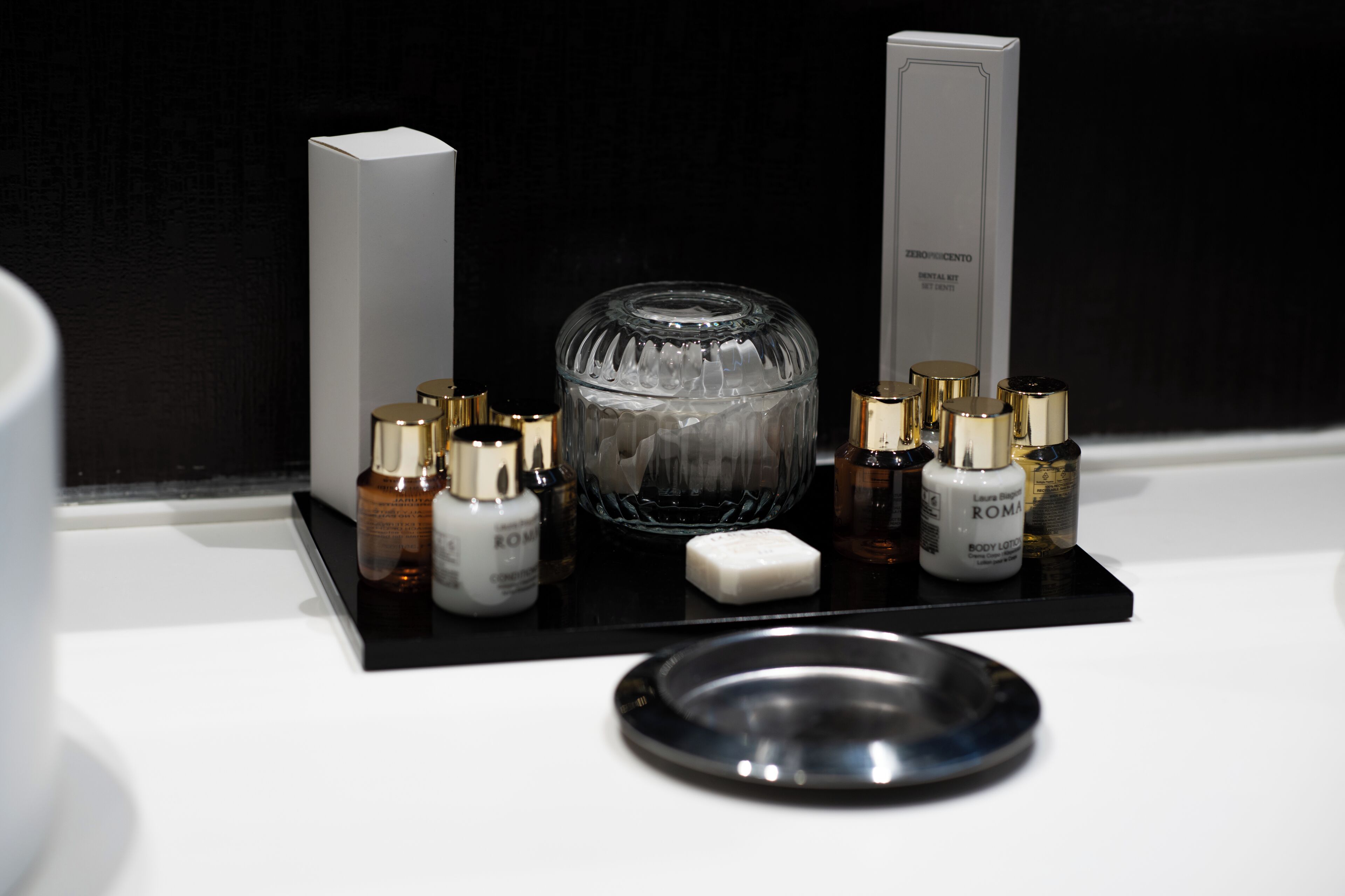 A bathroom vanity with a black tray holding various toiletries, a glass container, and a soap bar.