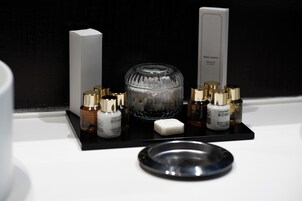 Et badeværelsesbord med en sort bakke, der indeholder forskellige toiletartikler, et glas og en sæbe.