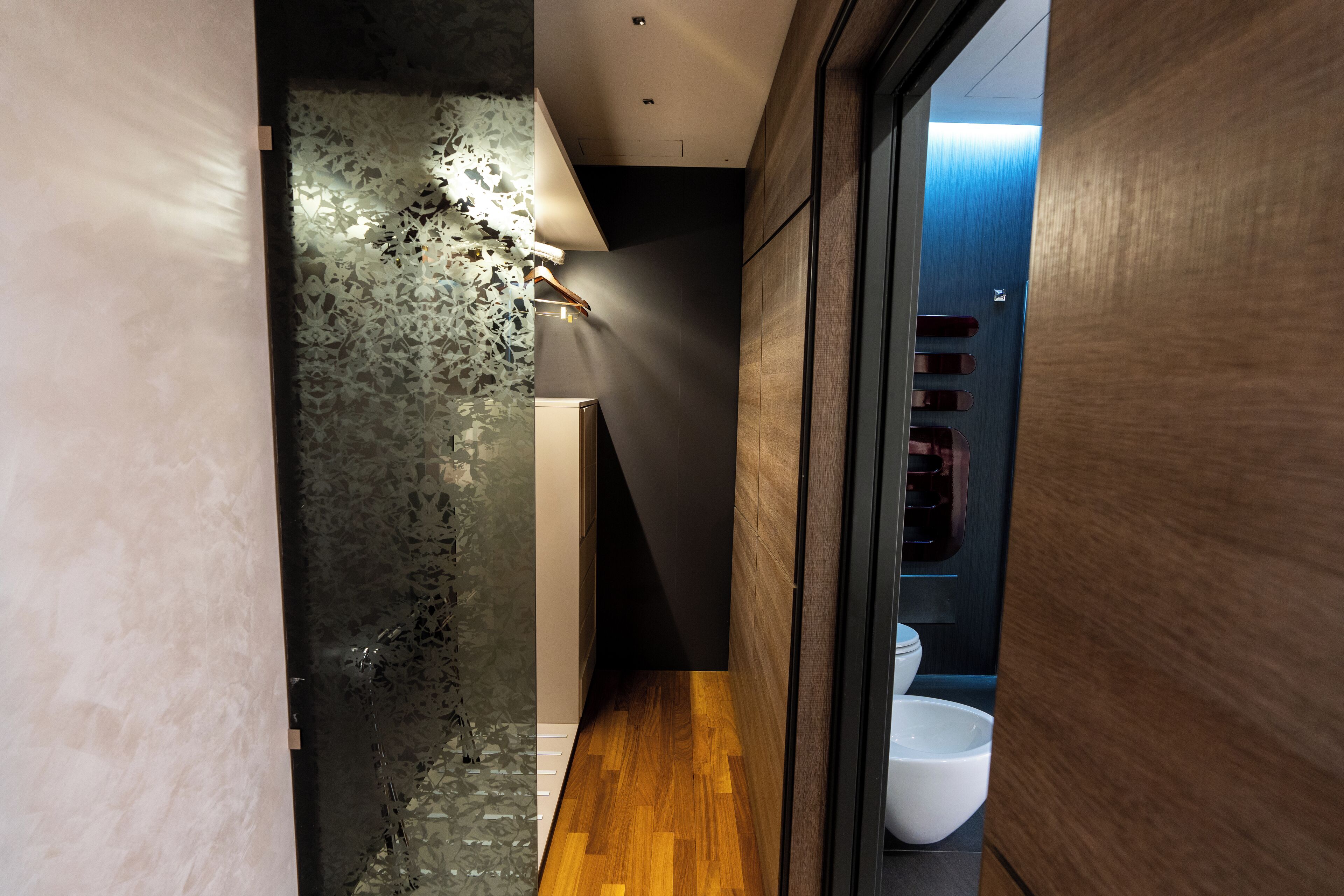 Un pasillo estrecho con suelo de madera, pared blanca con textura y puerta de madera con manija.