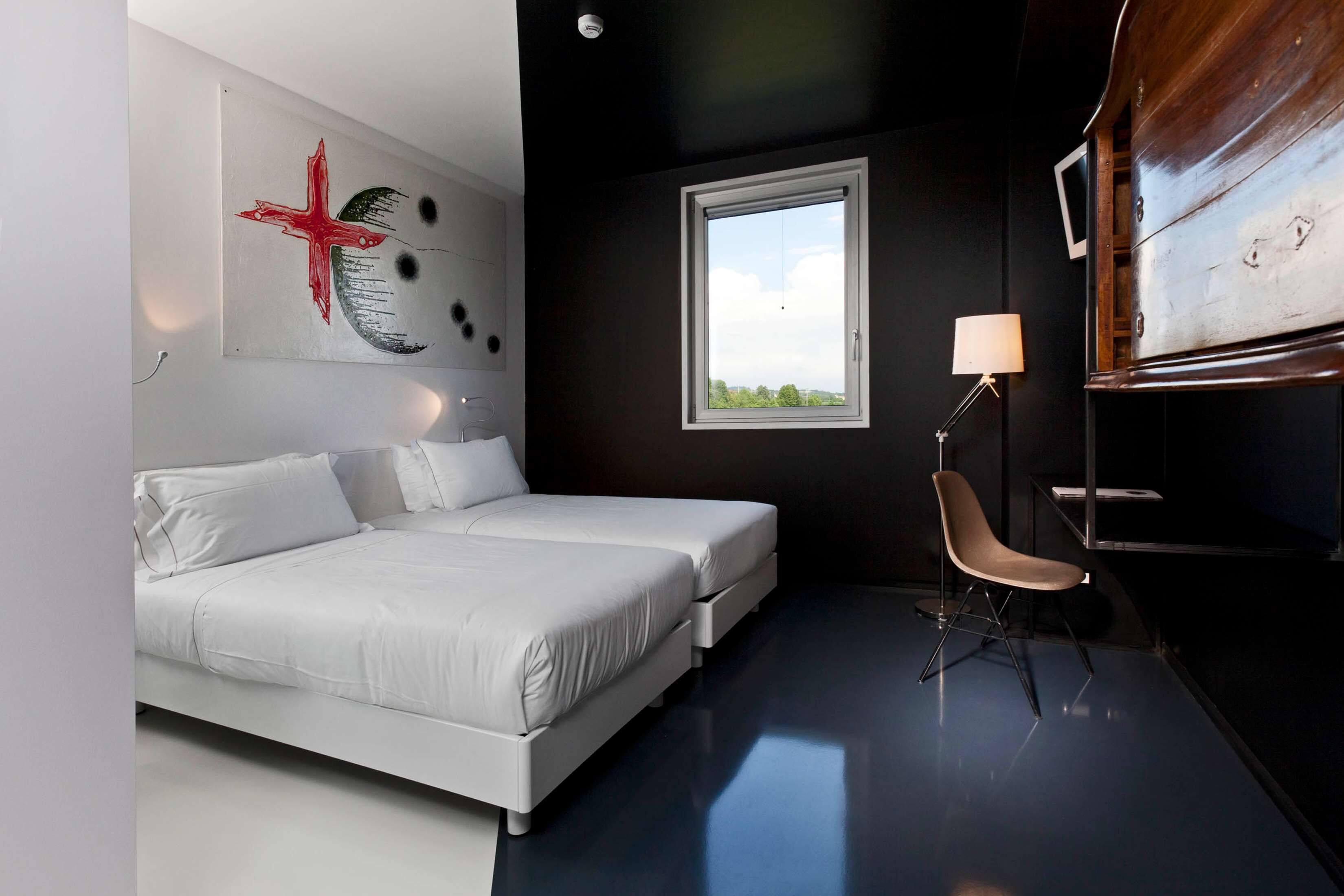 A modern bedroom with a bed, a chair, a window, and a wall with a red abstract painting.