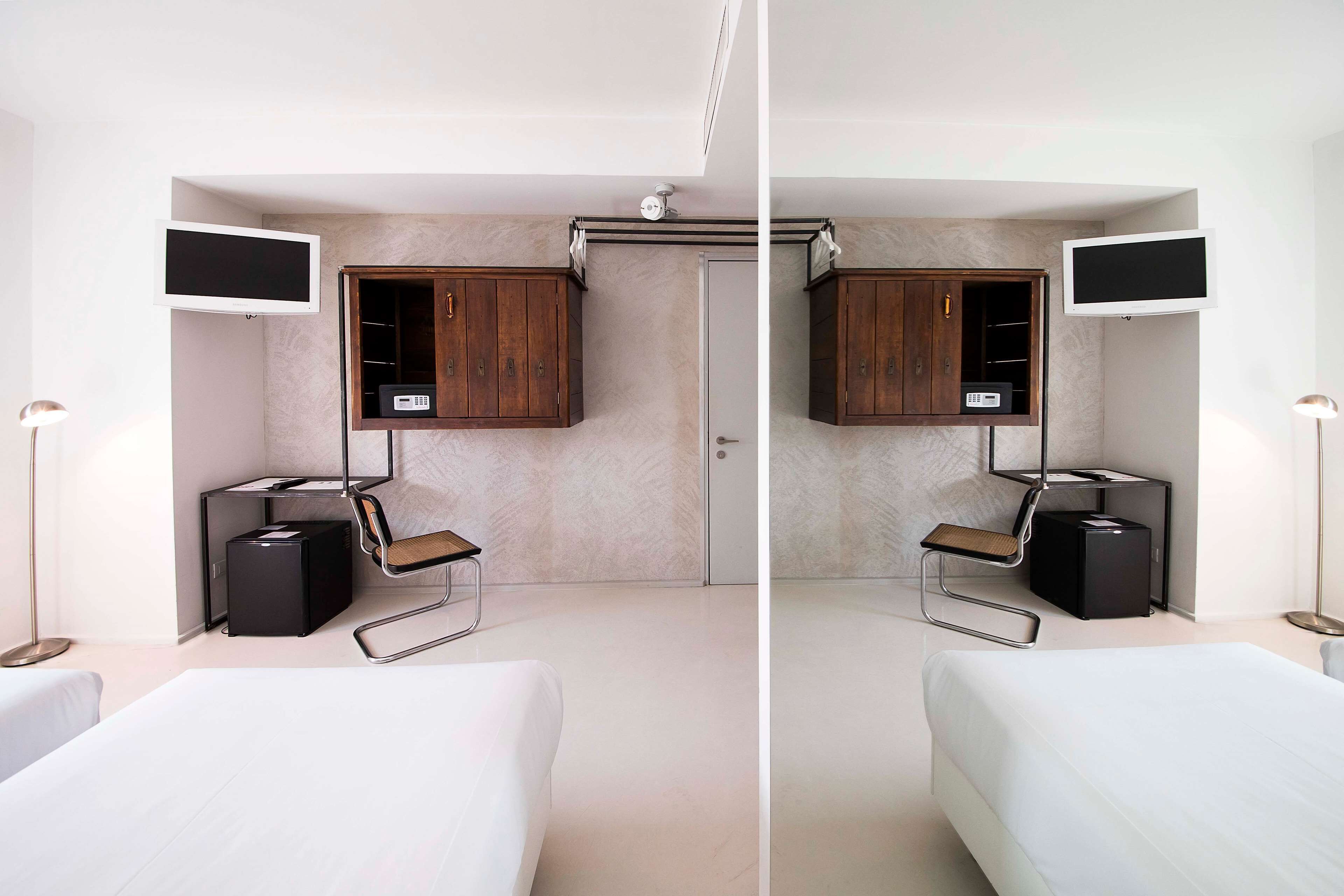 A modern hotel room with two beds, a minibar, a desk with a chair, and a television mounted on the wall.