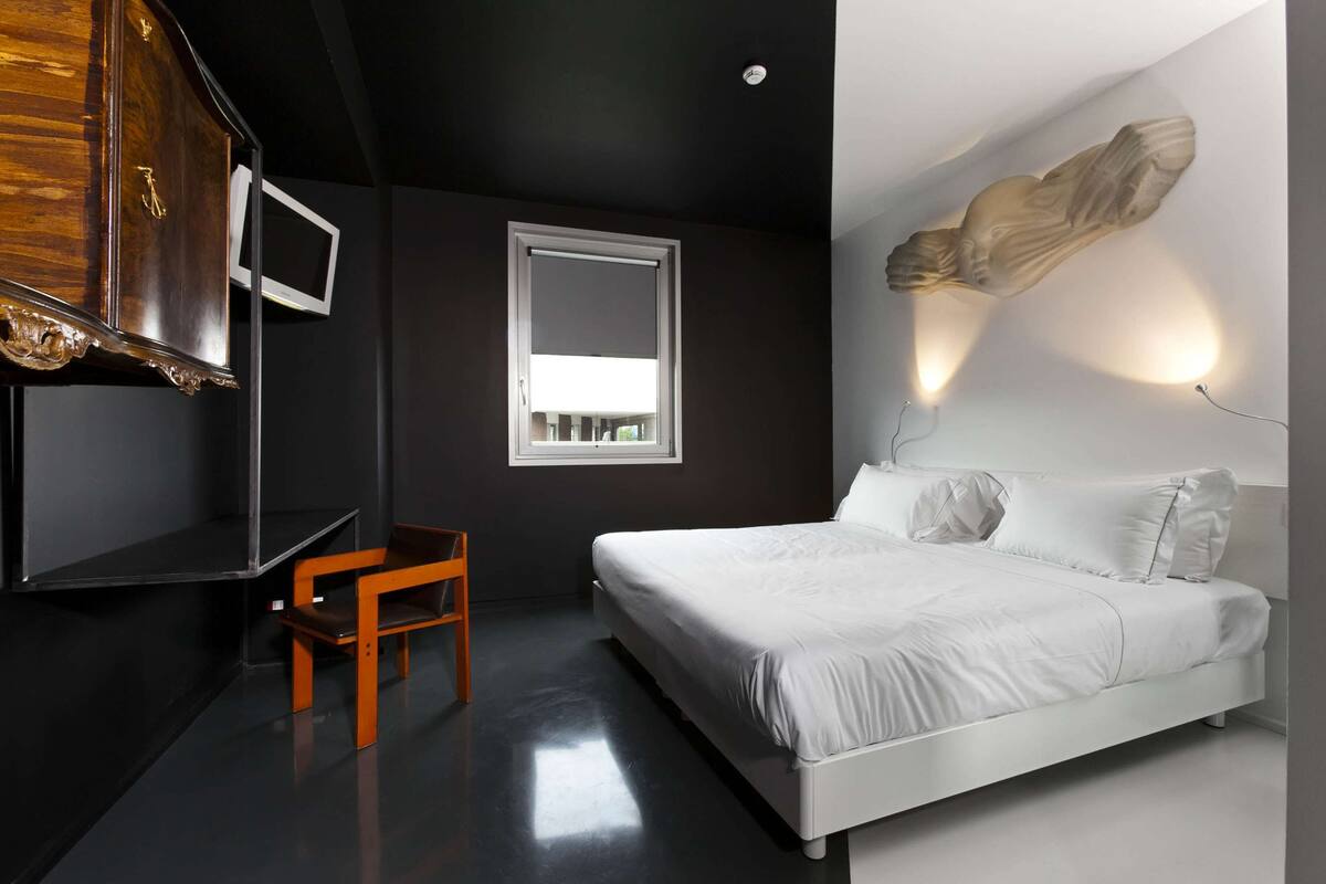 Une chambre à coucher moderne avec un lit blanc, une chaise en bois, une armoire et une sculpture fixée au mur.