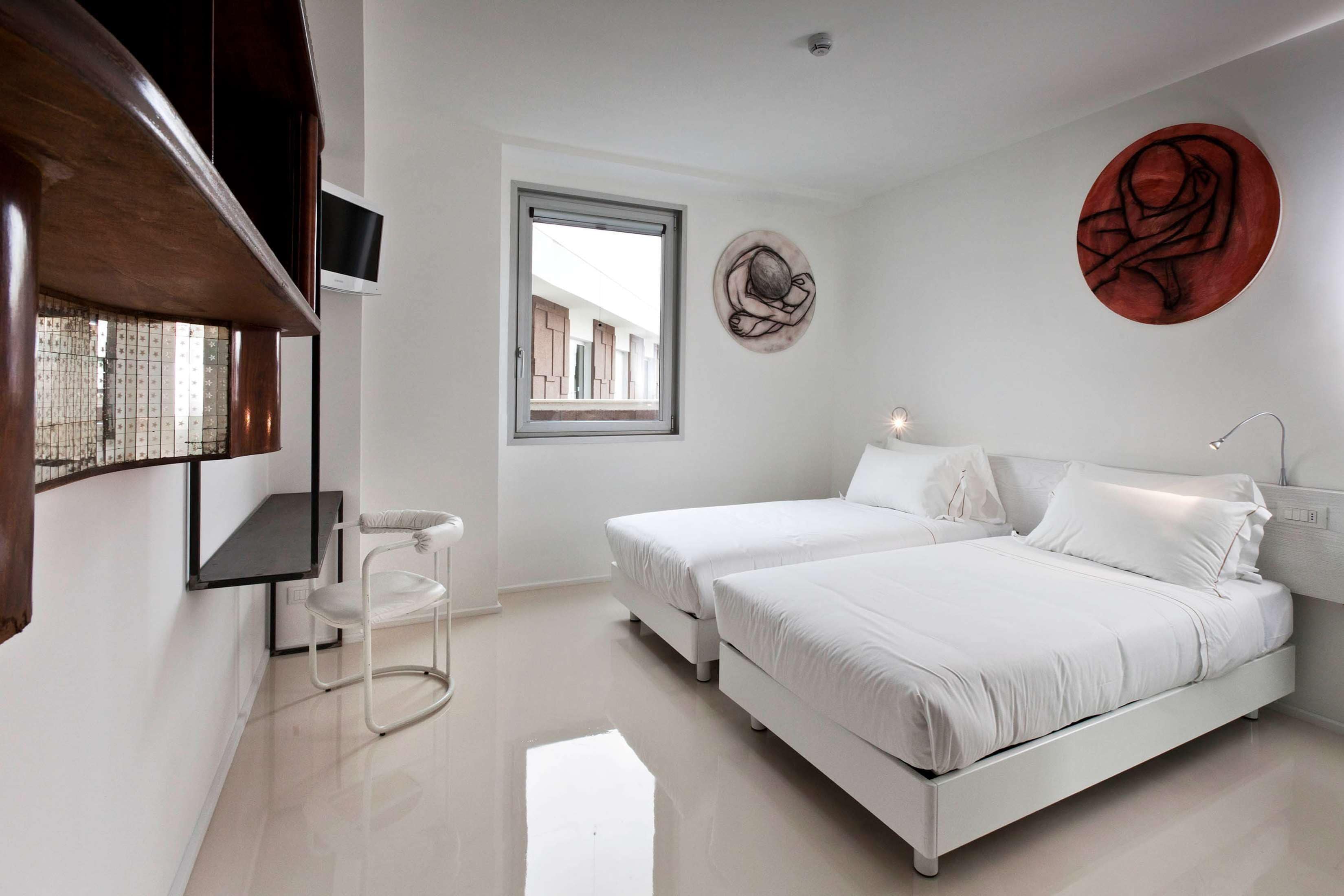 A modern bedroom with two beds, a window, and a wall-mounted artwork.
