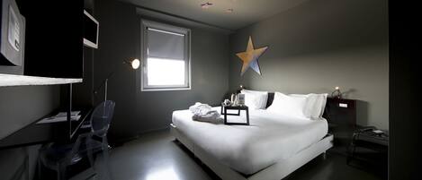 Une chambre d’hôtel moderne avec un grand lit, un bureau et une chaise. Il y a une fenêtre et une décoration en forme d’étoile au plafond.
