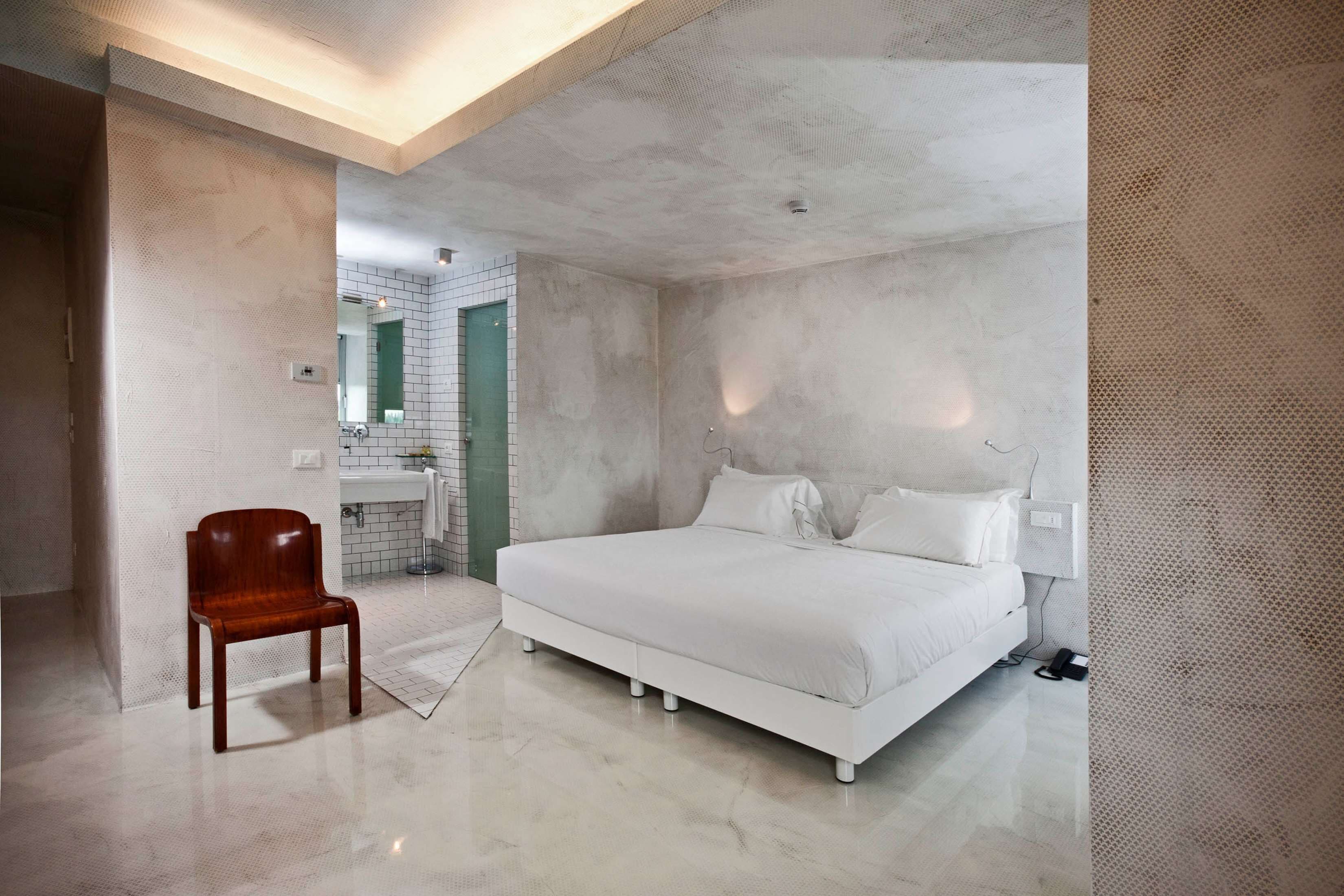 Un dormitorio moderno con una cama grande, una silla de madera y un baño visible a través de una puerta abierta.