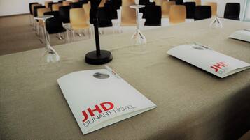 Una sala conferenze con un tavolo apparecchiato per una riunione, comprensivo di cartellini di nome, un microfono e una brochure per l'Hotel JHD Dunant.