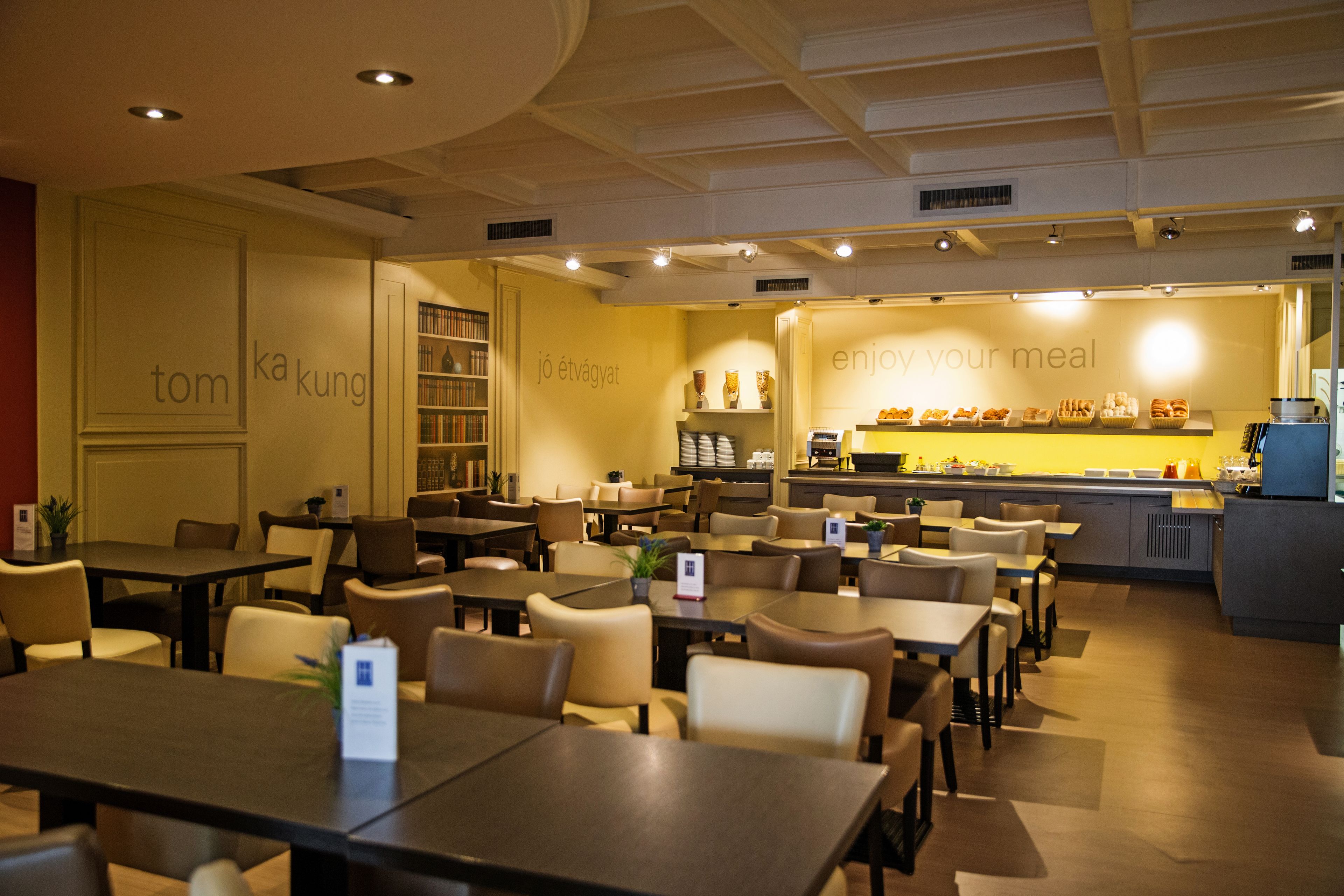 Un restaurante con varias mesas y sillas, una zona de cocina y estanterías con distintos objetos.