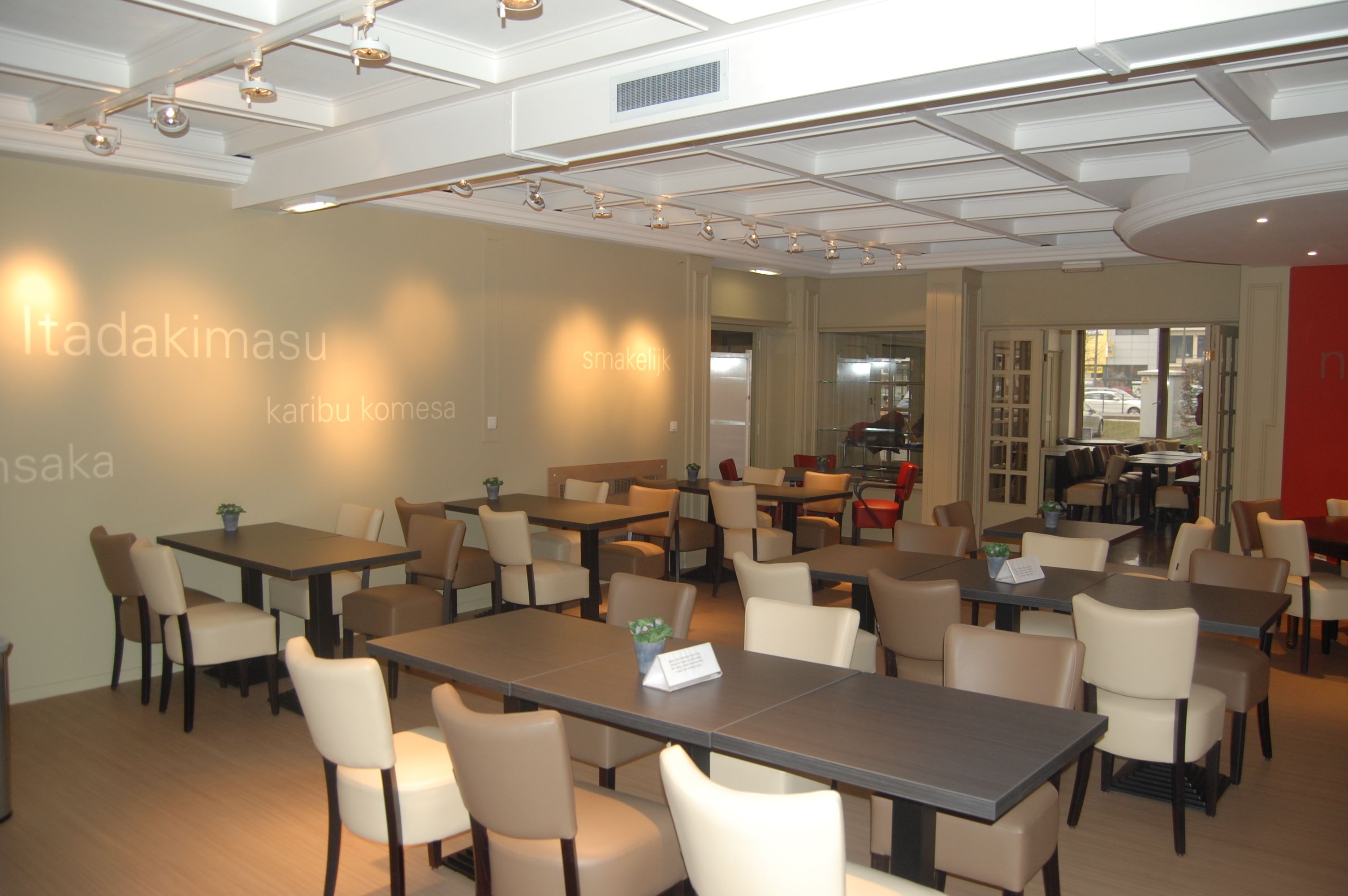 Une salle de conférence équipée de tables et de chaises, un plafond doté d’un éclairage encastré et un mur portant des panneaux d’affichage.
