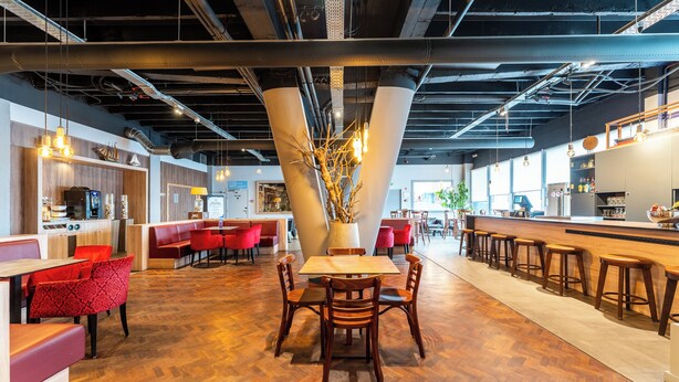 A modern restaurant with wooden flooring, red and black chairs, and a central table with a vase of branches. - Antwerp Harbour Hotel (Antwerp)