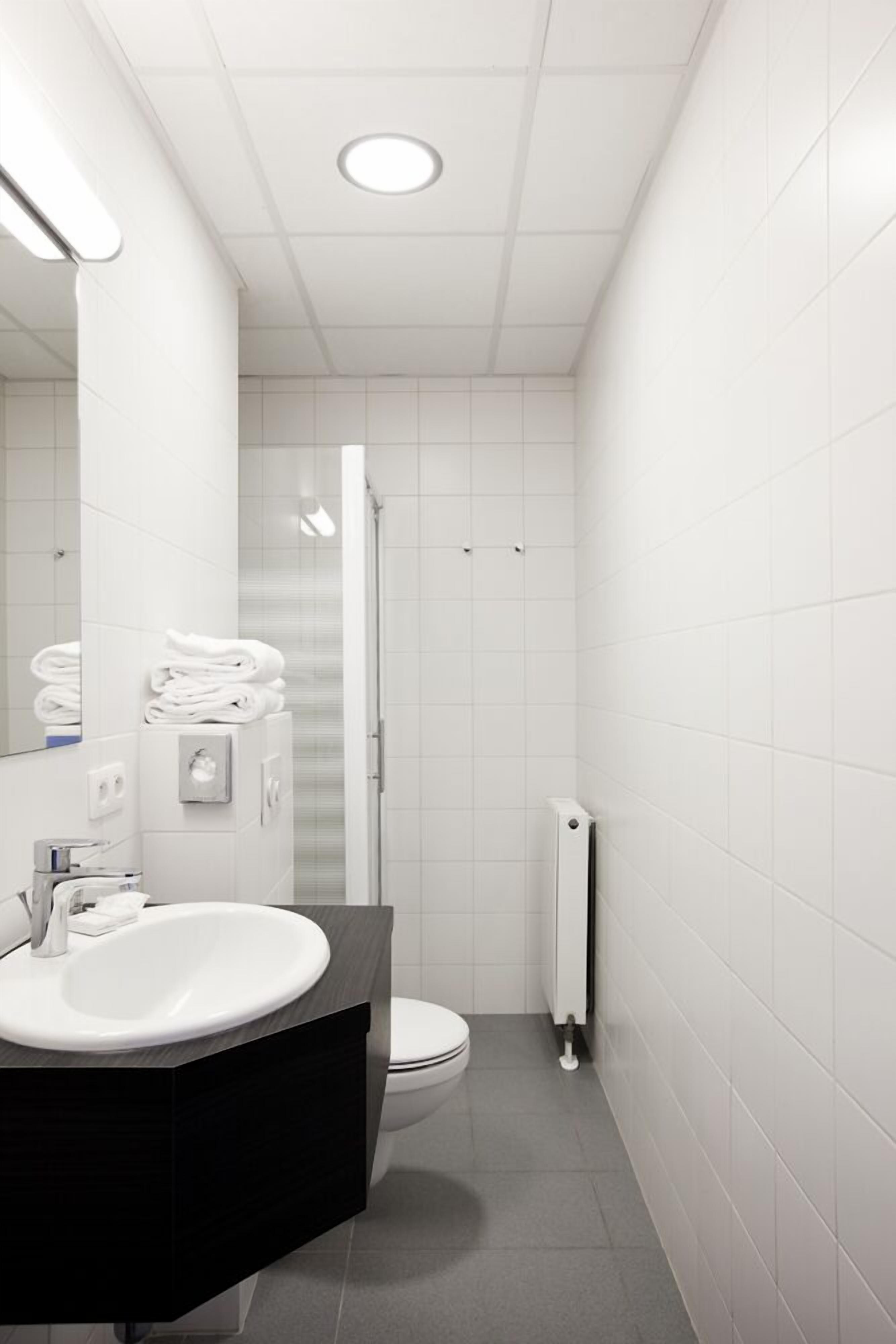 A modern bathroom with a white sink, mirror, and toilet.