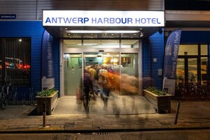 The exterior of the Antwerp Harbour Hotel with a clear sign, glass doors, and a bike parking area.
