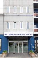 Exterior do Hotel Antwerp Harbour, com fachada moderna, grande entrada de vidro e uma placa.