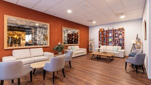 A spacious living area with a large sofa, two armchairs, a coffee table, and a bookshelf filled with books and decorative items. - Antwerp Harbour Hotel (Antwerp)