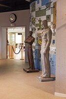 A hallway with two statues, a clock, and a mosaic wall.