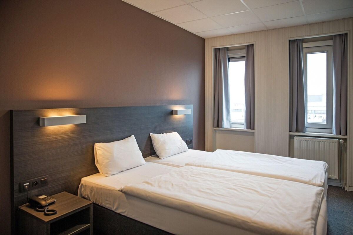 A hotel room with two beds, a bedside telephone, and a window with curtains.