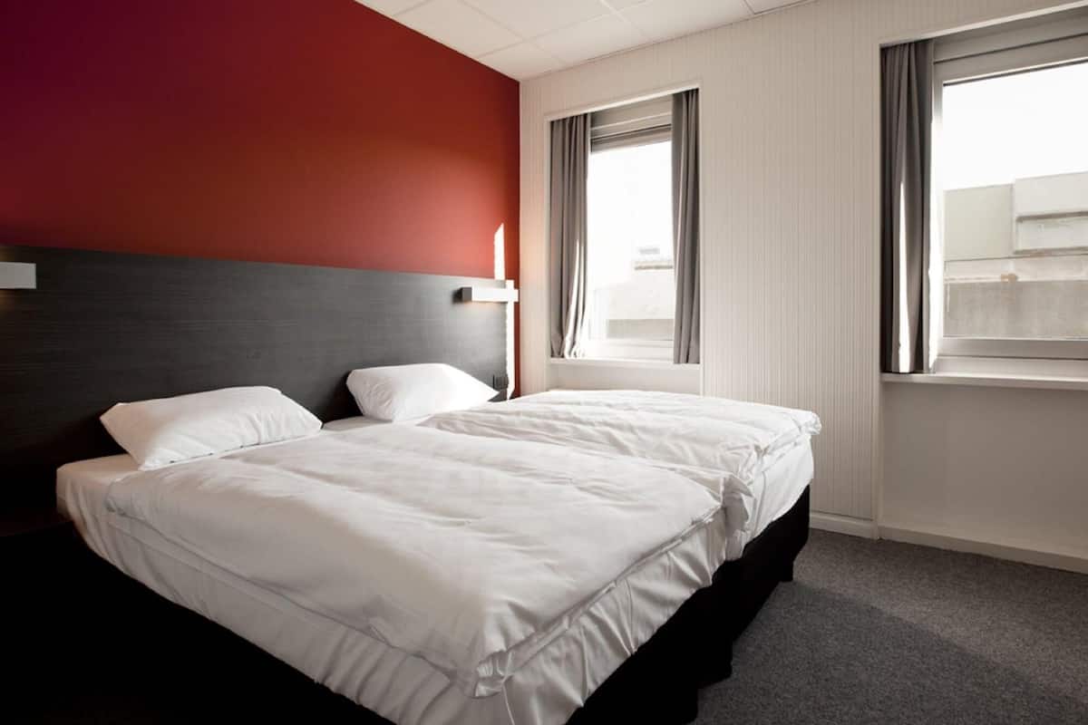 A hotel room with a large bed, a headboard, and a window with curtains.