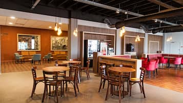 A modern restaurant with wooden tables and chairs, a bar area, and seating with orange and red chairs.