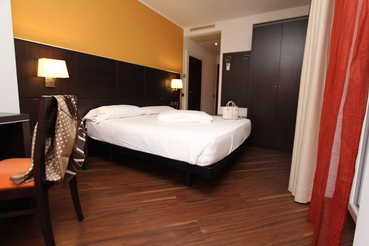 A hotel room with a bed, a chair, a desk, and a wardrobe.
