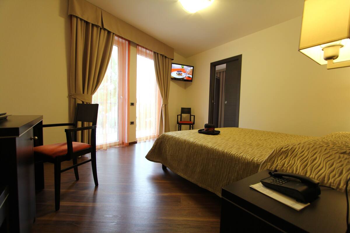 A hotel room with a bed, a desk, a chair, a television on the wall, and a telephone on the bedside table.