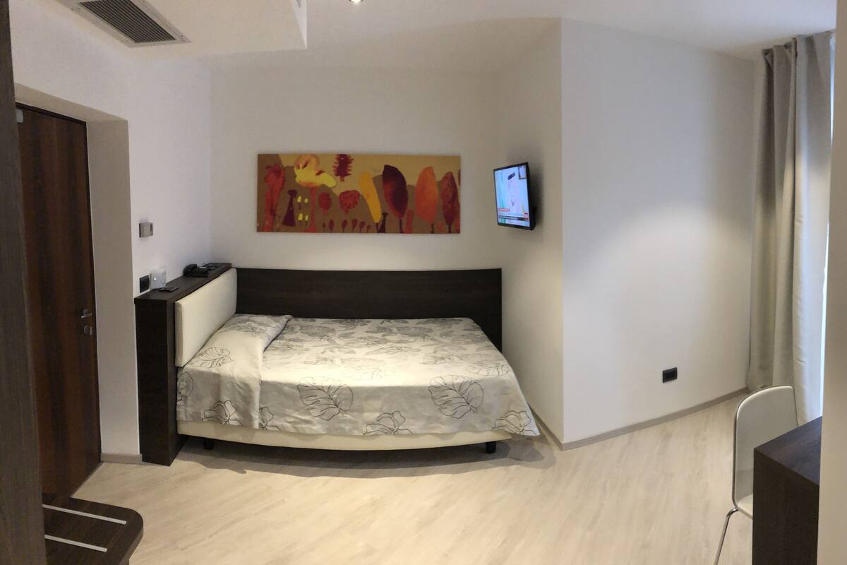 A bedroom with a bed, a TV mounted on the wall, and a painting above the bed.