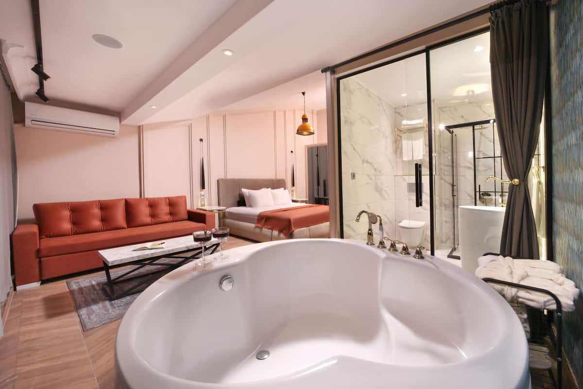 A modern hotel room with a large bathtub, a sofa, a coffee table, and a separate bedroom area.