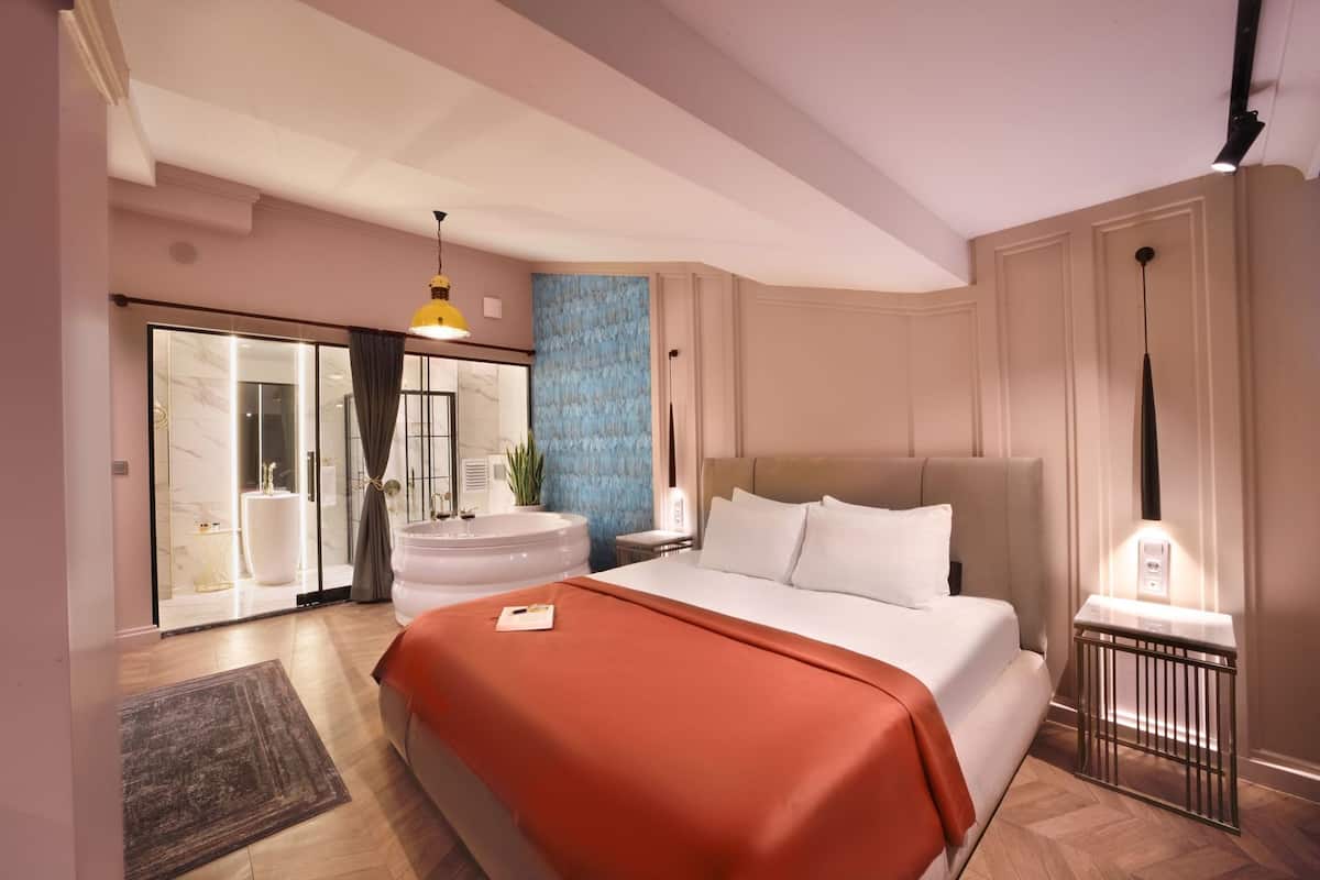 A modern hotel room with a large bed, a bathroom with a glass shower enclosure, and a blue accent wall.