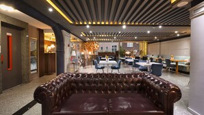 A modern hotel lobby with a leather sofa, dining area, and a ceiling with linear lighting. - Harbiye Residence (Istanbul)