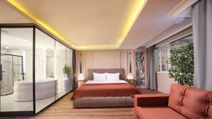 A modern bedroom with a large bed, bedside tables, a sofa, and a glass-enclosed bathroom. - Harbiye Residence (Istanbul)