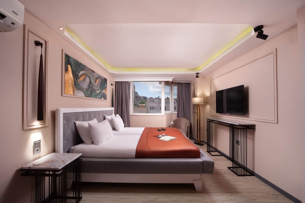 A hotel room with a large bed, a flat-screen TV, a desk, and a window with a city view.