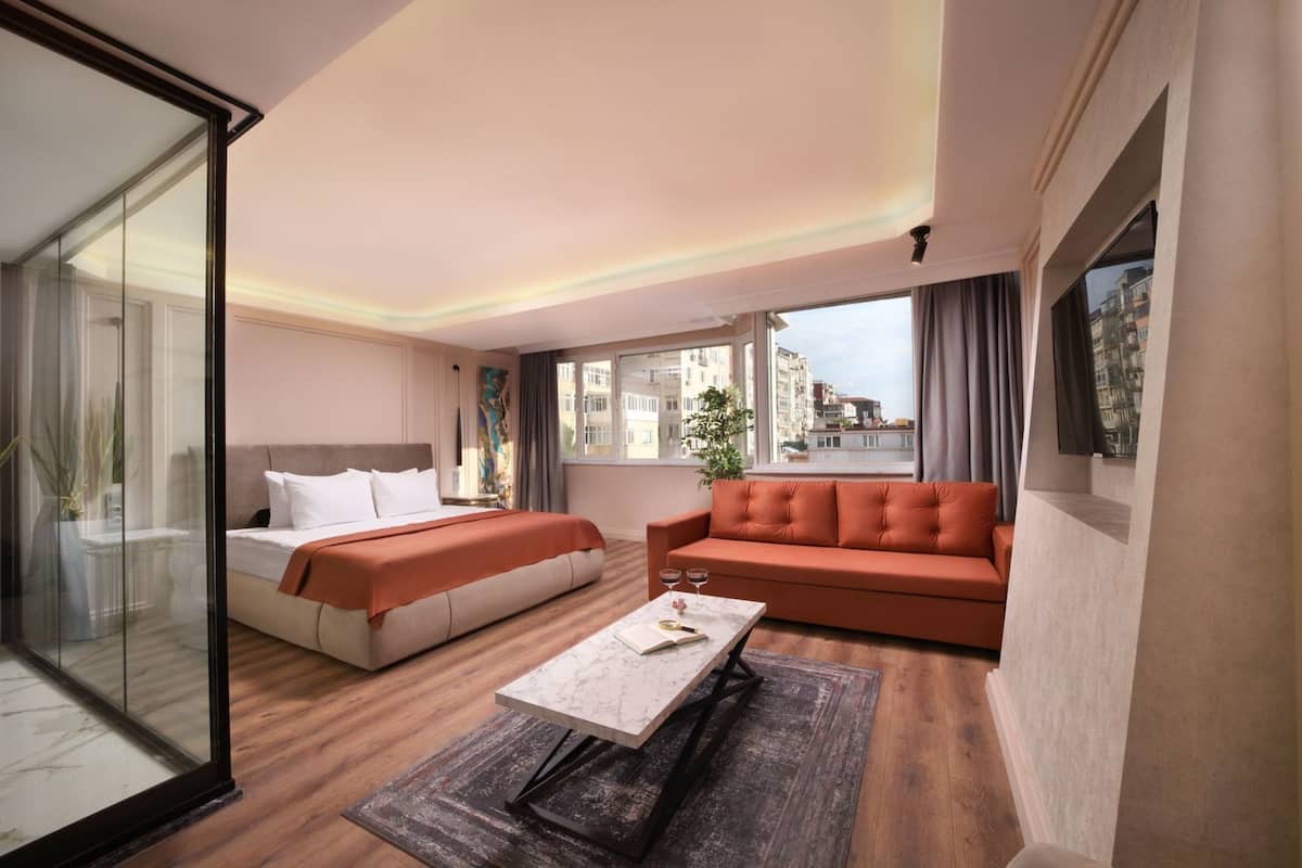 A hotel room with a bed, a sofa, a coffee table, and a view of buildings.
