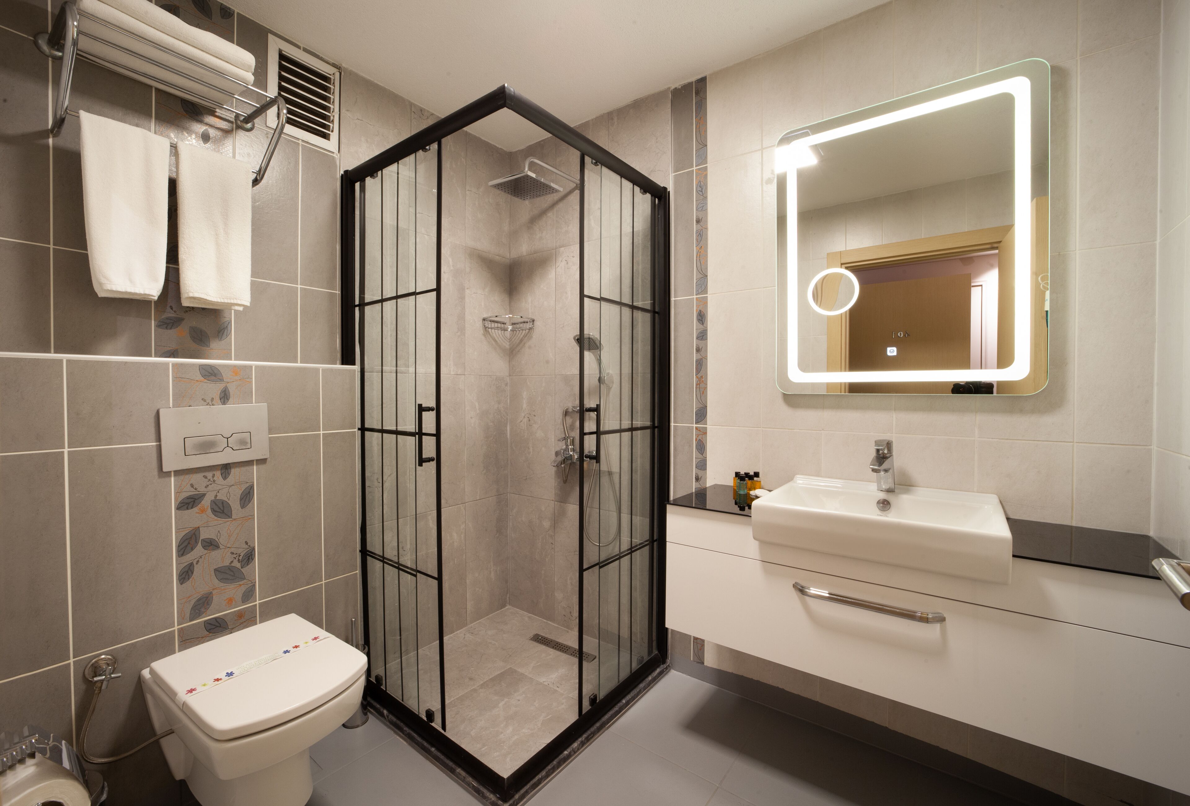 A modern bathroom with a glass-enclosed shower, a toilet, a sink with a mirror, and towels on a rack.