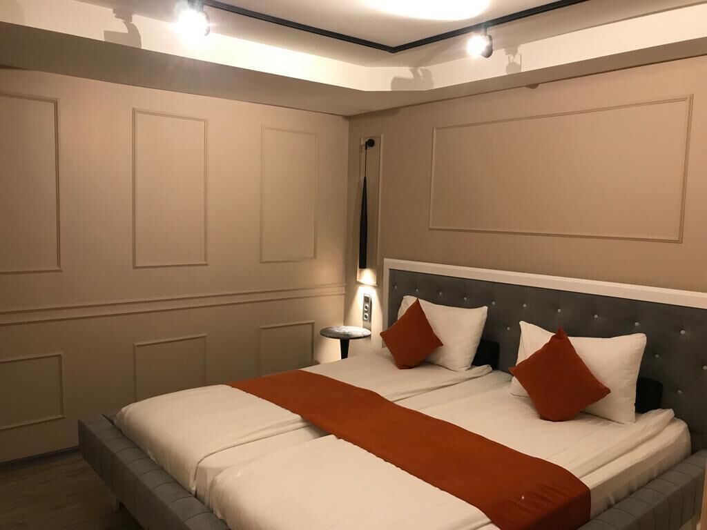 A bedroom with a large bed, a nightstand, and a wall-mounted lamp.