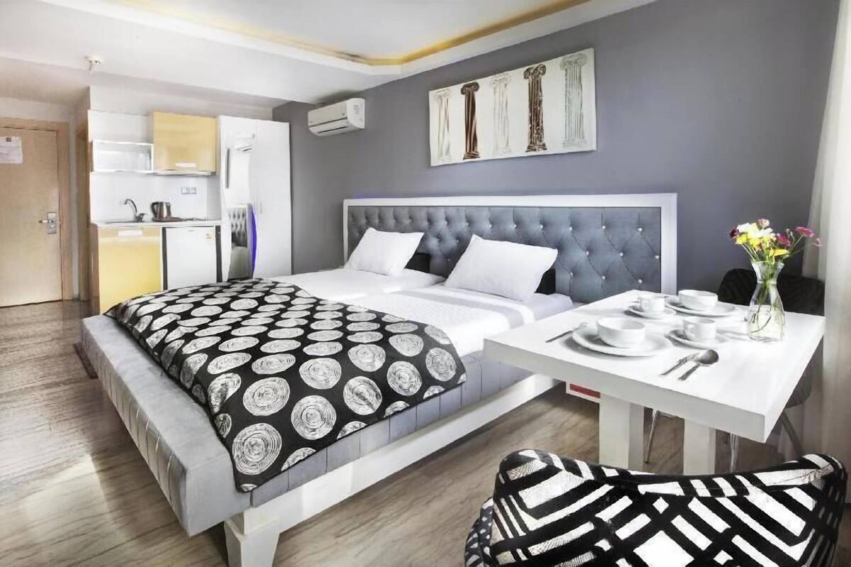 A modern hotel room with a bed, bedside table, and a small dining area.