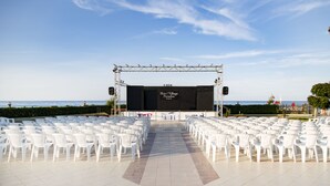 An outdoor stage with rows of white plastic chairs arranged for an event. - Hotel Village Paradise (Mandatoriccio)