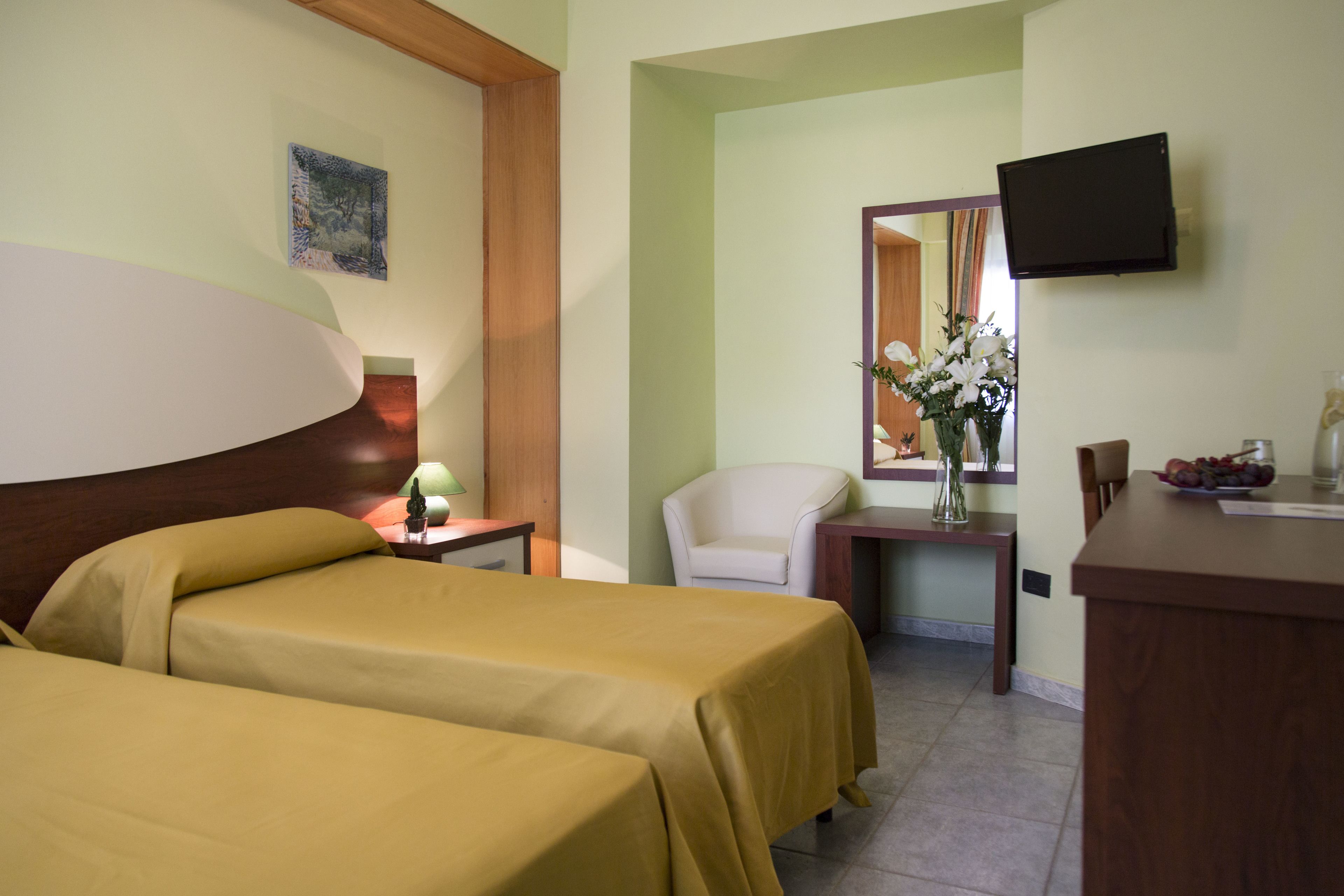 Habitación de hotel con dos camas, un escritorio, una silla, un televisor y un florero con flores.