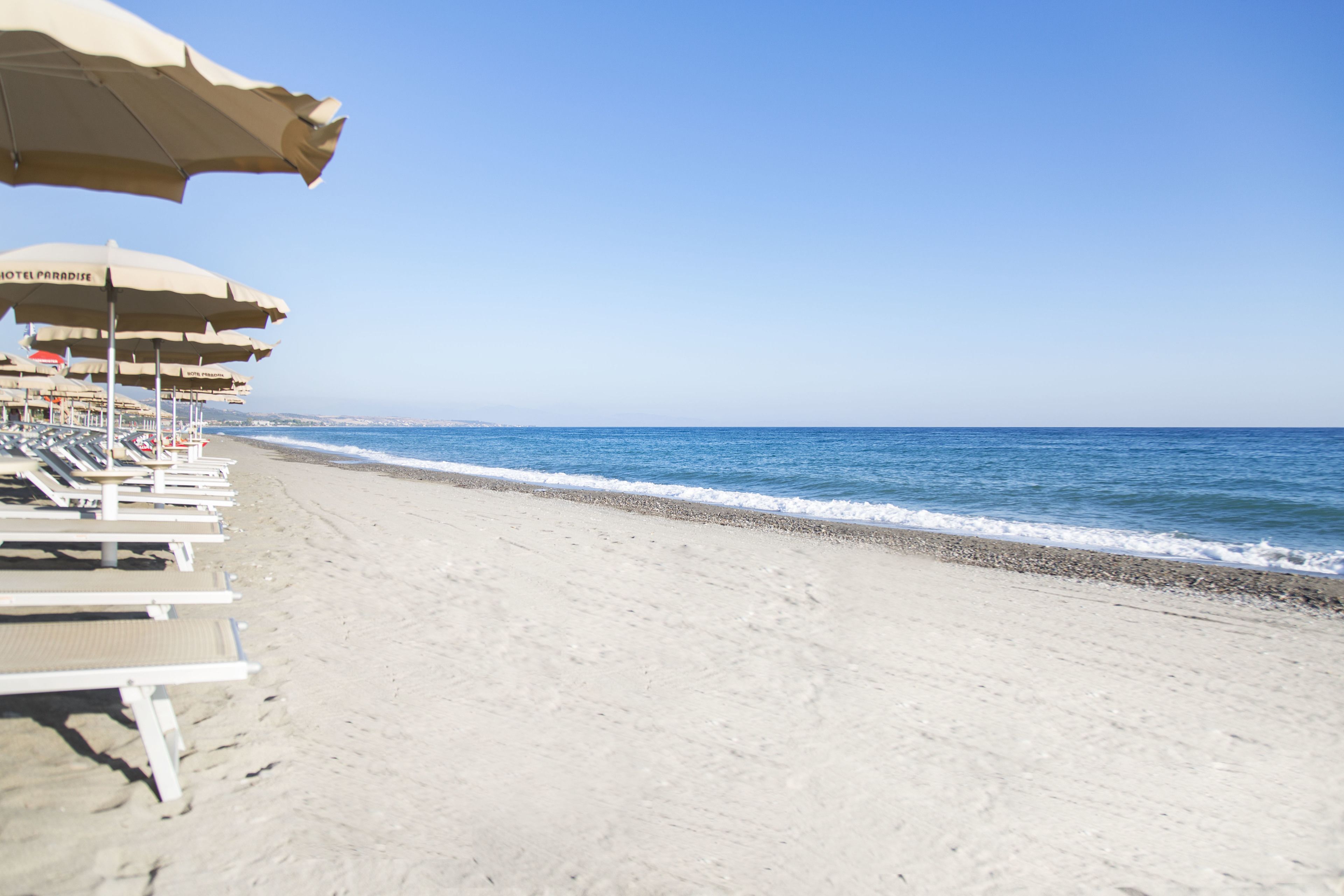 A beach with sun loungers and umbrellas, a clear sky, and the ocean.