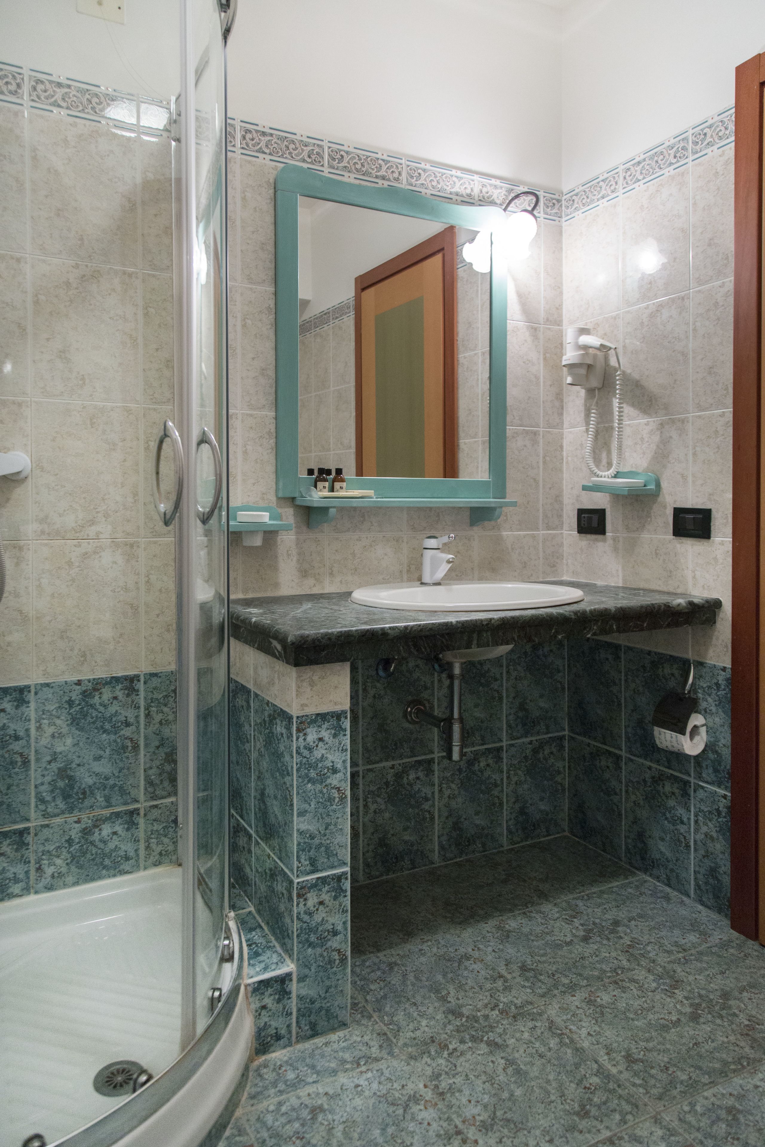 Un baño con cabina de ducha de vidrio, un lavamanos con espejo y un inodoro con dispensador de toallas de papel.