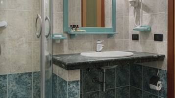 Un baño con cabina de ducha de vidrio, un lavamanos con espejo y un inodoro con dispensador de toallas de papel.