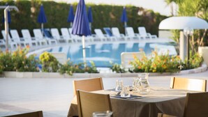 A poolside dining area with a table set for two, surrounded by lounge chairs and umbrellas. - Hotel Village Paradise (Mandatoriccio)