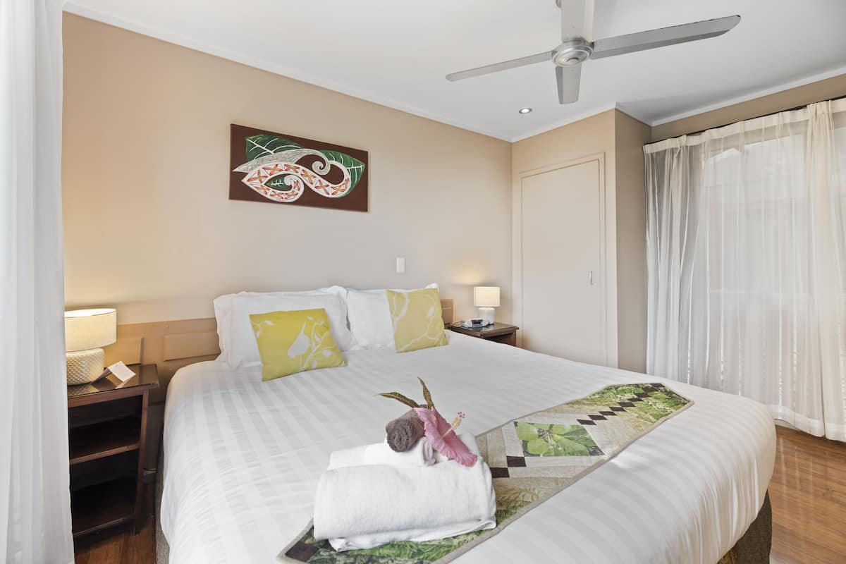 Ein Hotelzimmer mit einem großen Bett, einem Deckenventilator, einem Nachttisch mit Lampe und einem Bild an der Wand.